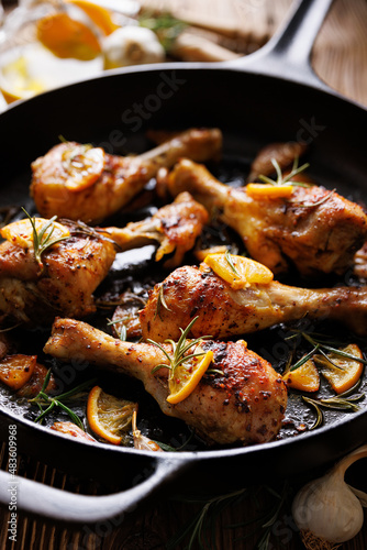 Roasted chicken legs, drumsticks with rosemary, garlic and lemon in a cast iron skillet, close up view