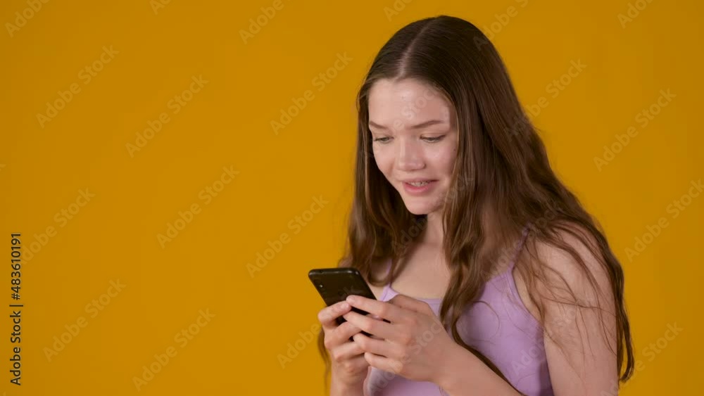 Young blonde girl using smart phone and texting online chat with smile isolated on yellow background. People lifestyle concept. Young blonde girl using smart phone and texting online chat with smile isolated on yellow background. People lifestyle concept.