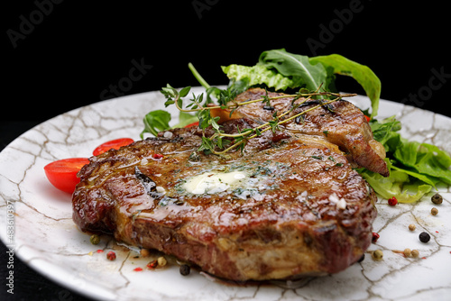 Grilled meat steak with butter, herbs and cherry tomatoes on a white plate, against a dark background