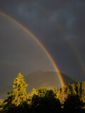 Rainbow on cloudy sky with mountain peaks in background. Summer landscape after storm.  .