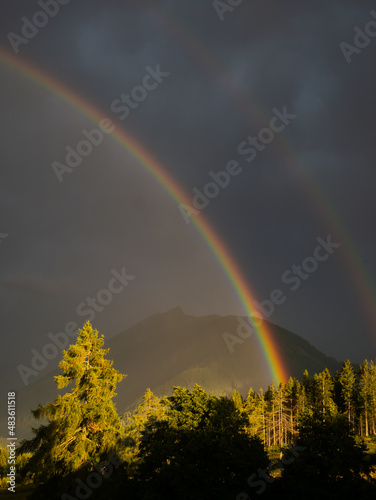 Fototapeta Naklejka Na Ścianę i Meble -  Rainbow on cloudy sky with mountain peaks in background. Summer landscape after storm.  .