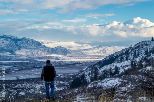 Man Looks Out Over Snow Covered Mountain Valley with Blue Sky and Fluffy Clouds
