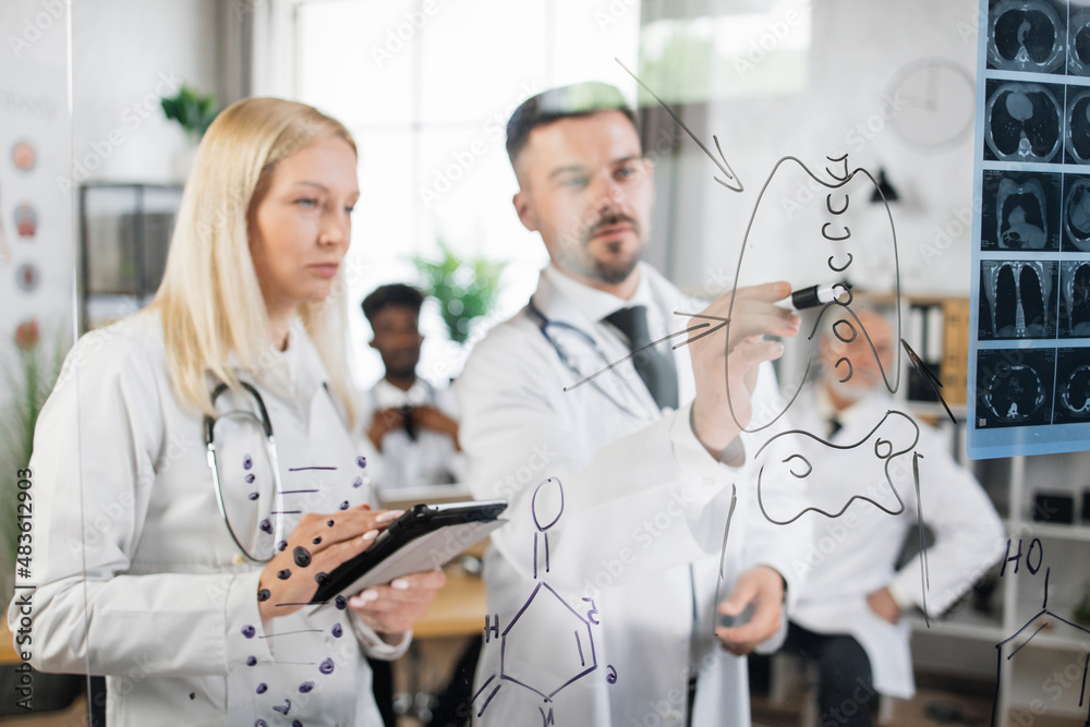 Obraz premium Team of qualified medical scientists using tablet and writing on glass flip chart during meeting at hospital room. Clinical studies and cooperation concept.