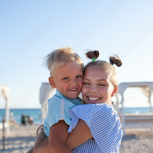 Murais de parede Happy older sister and younger little brother run on the sand, play and hug on the seashore