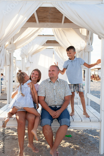 portrait of a big happy family, parents with children are relaxing on the seashore, they are sitting in a bungalow
