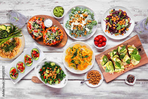 Healthy plant based low carb food table scene. Top down view on a white wood background. Cauliflower flatbread and steak, vegetable noodles, kale salads, stuffed avocados and sweet potatoes.