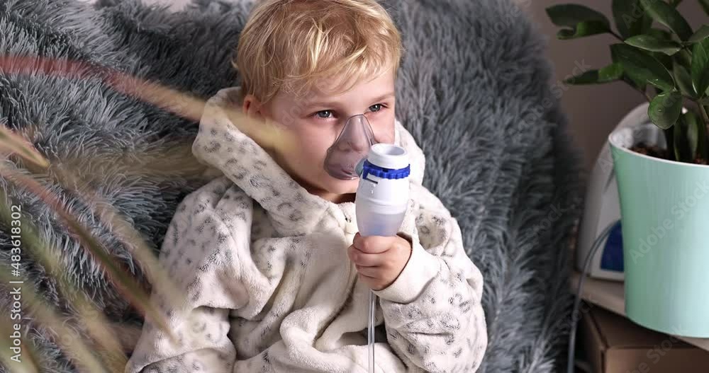 Cute baby boy makes inhalation with a nebulizer equipment. Sick child holding inhalator in hand and breathes through an inhaler at home. Physical therapy for cold, flu and bronchial asthma Cute baby boy makes inhalation with a nebulizer equipment. Sick child holding inhalator in hand and breathes through an inhaler at home. Physical therapy for cold, flu and bronchial asthma