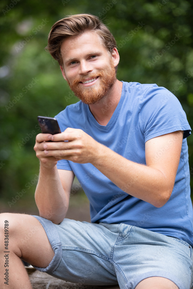 young man addicted to his phone in the forest young man addicted to his phone in the forest