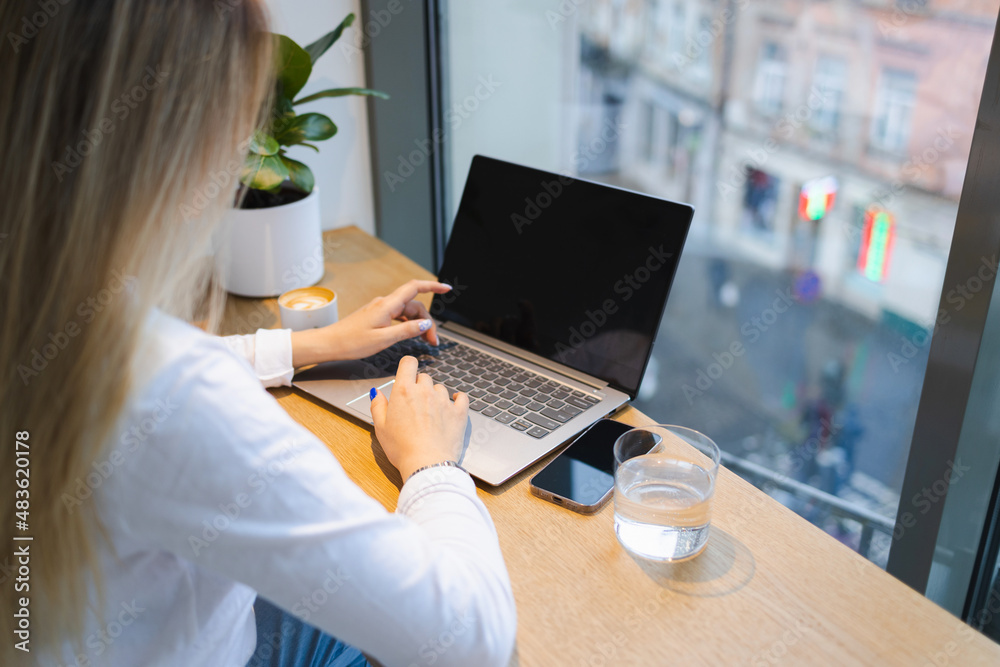 Back view of unrecognizable woman working on laptop at table in cafe