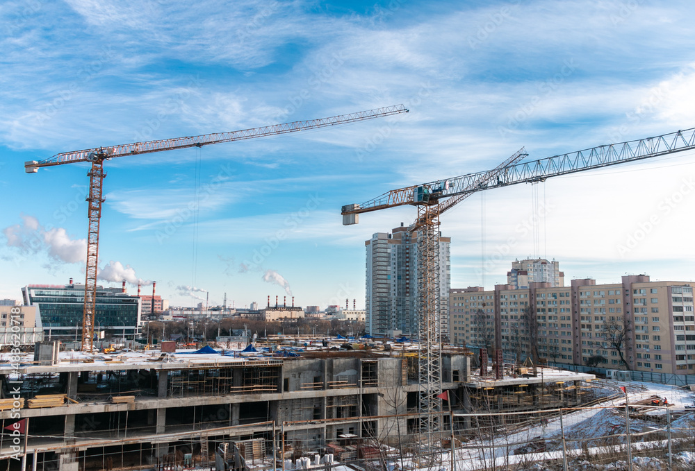 Construction cranes at a construction site in the city against the blue sky in winter conditions. The concept of building a new area. Construction of a new building. Construction cranes at a construction site in the city against the blue sky in winter conditions. The concept of building a new area. Construction of a new building.