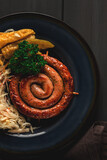 Traditional German dish, Fried spiral sausage, with sauerkraut,with red sauce, on a dark gray wooden background, top view, horizontal, no people,
