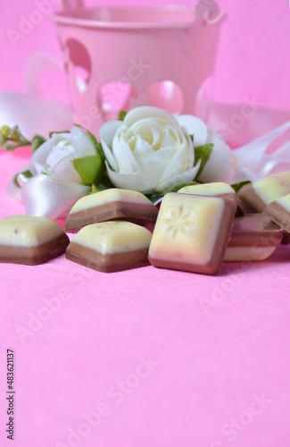 Decorative flowers and pieces of chocolate on a pink background. Valentine's Day