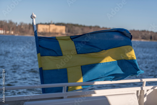 Swedish flag at the aft of a commuting boat with skyline of the island Djurgården in the background a sunny winter day in Stockholm