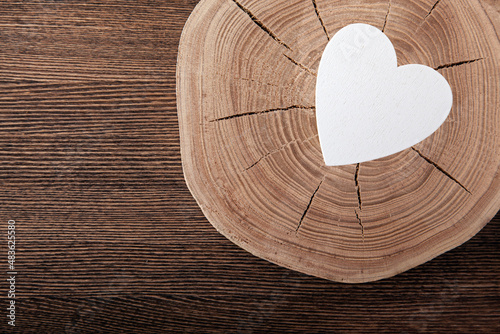 White wooden heart on a saw cut with annual rings and cracks on a wooden background. Neutral brown background. Eco concept for valentine's day