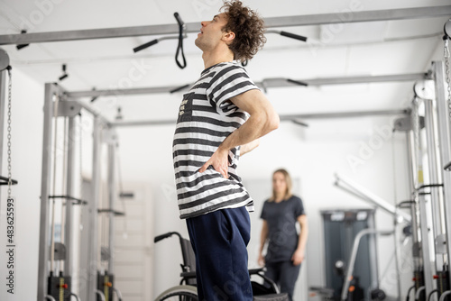 Guy feeling back pain while exercising in a rehabilitation center. Concept of physical therapy and kinesiology for muscle recovery and strengthening