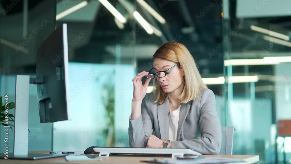 Overworked tired lady holding glasses feeling headache, having eyesight problem after computer work. Stressed mature employee business woman suffering fatigue rubbing dry eyes at workplace in office