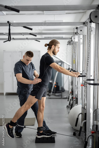 Fototapeta Naklejka Na Ścianę i Meble -  Man doing exercises on decompression simulators with the help of rehabilitation specialist. Concept of physical therapy for health and recovery. Idea of kinesiology in the treatment of back
