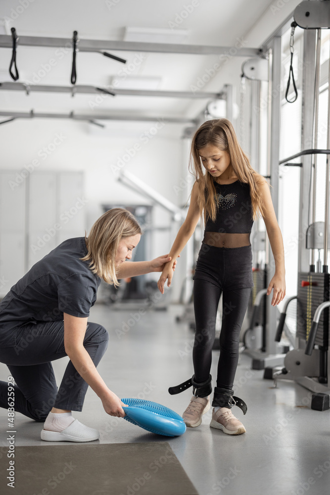 Rehabilitation specialist helping little girl to do exercises at gym