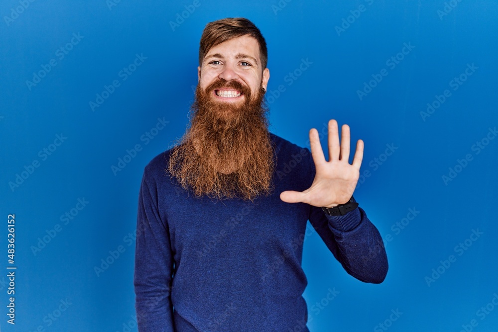 Naklejka premium Redhead man with long beard wearing casual blue sweater over blue background showing and pointing up with fingers number five while smiling confident and happy.