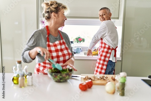 Senior caucasian couple smiling happy cooking at the kitchen.
