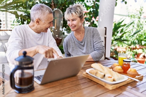 Senior caucasian couple smiling happy having breakfast and using laptop at the terrace.