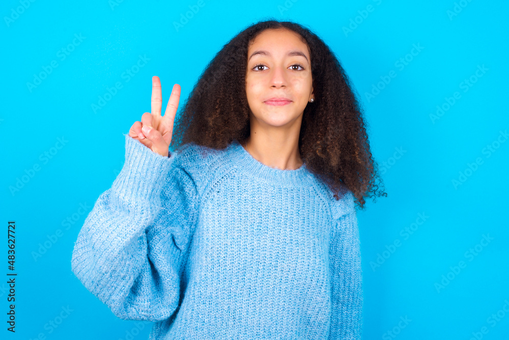 African teenager girl wearing blue sweater over blue background showing and pointing up with fingers number two while smiling confident and happy.