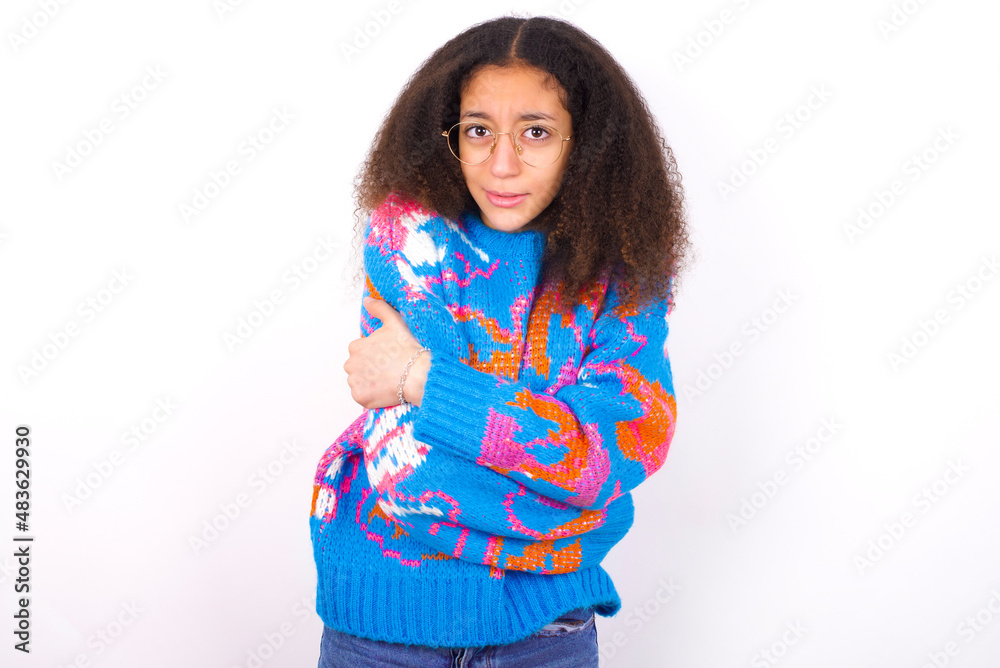 African teenager girl wearing colorful sweater over white background shaking and freezing for winter cold with sad and shock expression on face. African teenager girl wearing colorful sweater over white background shaking and freezing for winter cold with sad and shock expression on face.