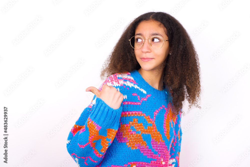 African teenager girl wearing colorful sweater over white background points away and gives advice demonstrates advertisement African teenager girl wearing colorful sweater over white background points away and gives advice demonstrates advertisement