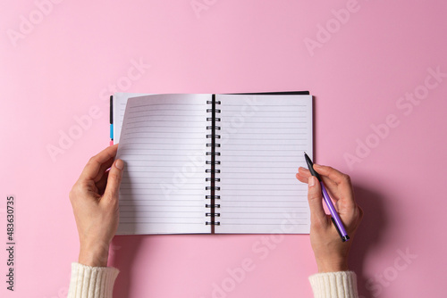 Foto Female hand writing in blank open spiral notebook with pen on pastel pink background