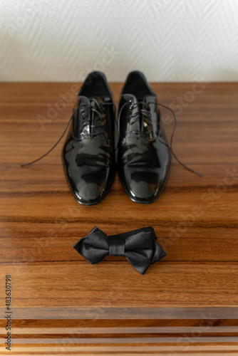 Patent leather groom shoes and bowtie over wooden furniture getting ready concept, vertical orientation