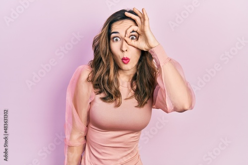 Young hispanic girl wearing casual clothes doing ok gesture shocked with surprised face, eye looking through fingers. unbelieving expression.