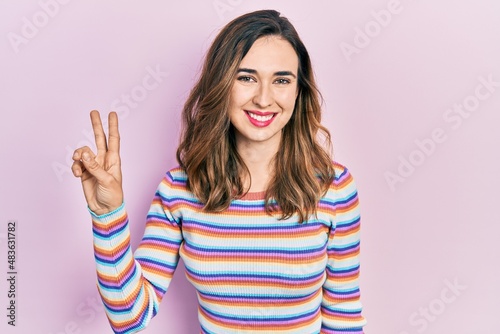 Young hispanic girl wearing casual clothes smiling looking to the camera showing fingers doing victory sign. number two.