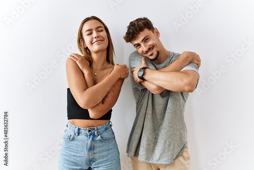 Young beautiful couple standing together over isolated background hugging oneself happy and positive, smiling confident. self love and self care