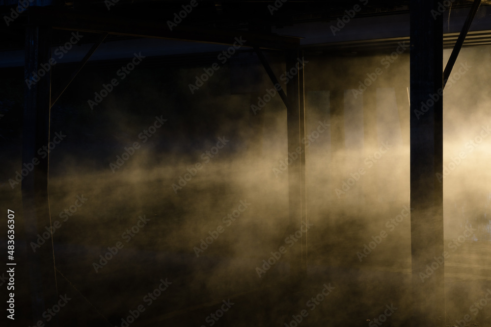 Bridge support beams in mist covered water at sunrise