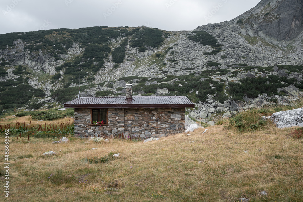 Scenic mountain hut made of stone with flowers on the window and a rocky hill in the background