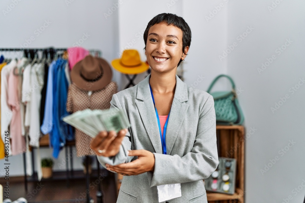 © Krakenimages.com - Young hispanic woman shopkeeper smiling confident holding dollars banknotes at clothing store