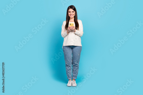 Full length photo of young cheerful girl use mobile share repost app download app isolated over blue color background