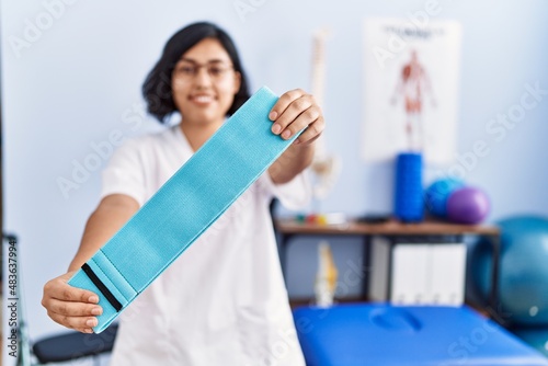 Young latin woman wearing physiotherapist uniform holding elastic band at physiotherapy clinic