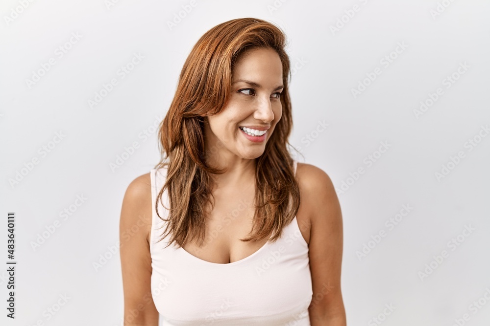 Middle age hispanic woman standing over isolated background looking away to side with smile on face, natural expression. laughing confident. Middle age hispanic woman standing over isolated background looking away to side with smile on face, natural expression. laughing confident.