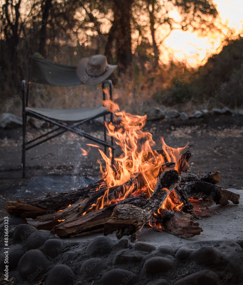 Lagerfeuer mit Stuhl und Hut im Sonnenuntergang Lagerfeuer mit Stuhl und Hut im Sonnenuntergang