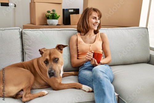 Young caucasian woman drinking coffee sitting on sofa with dog at home