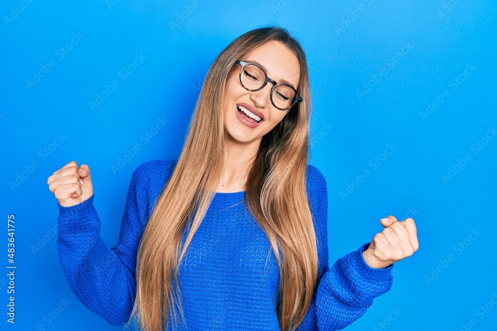 Fototapeta premium Young blonde girl wearing casual clothes and glasses very happy and excited doing winner gesture with arms raised, smiling and screaming for success. celebration concept.