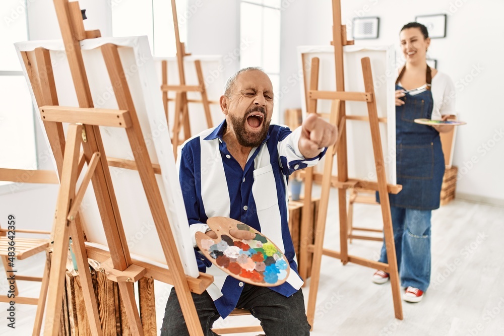 Senior artist man at art studio pointing displeased and frustrated to the camera, angry and furious with you Senior artist man at art studio pointing displeased and frustrated to the camera, angry and furious with you