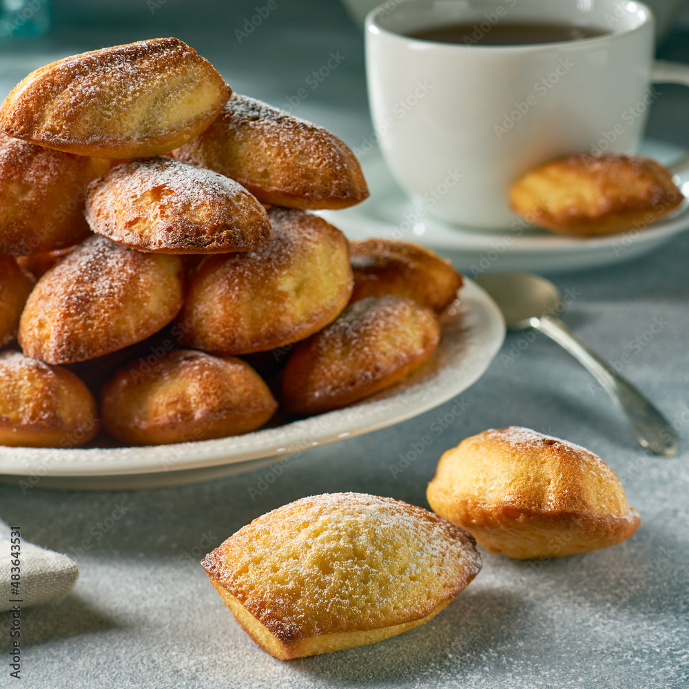 Heap of madeleine cookies on dish and tea on gray background