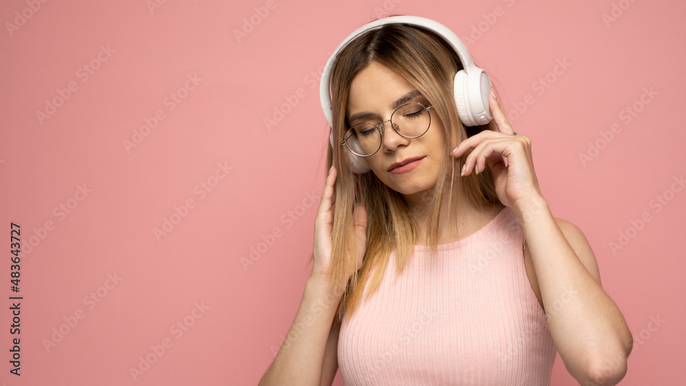 Young blonde beautiful girl in glasses in bright pink outfit enjoying a music on pink background. Young blonde beautiful girl in glasses in bright pink outfit enjoying a music on pink background.
