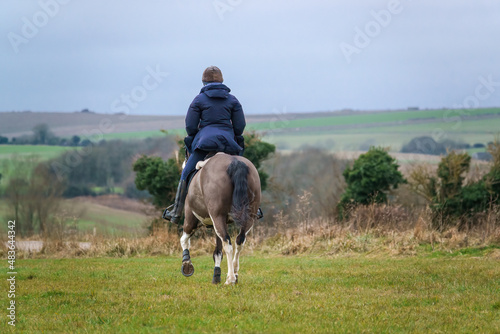 horse riding in open countryside under a blue grey cloud winter sky  © Martin