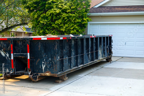 Long blue dumpster full of wood and other debris in the driveway in front of a house in the suburbs that is being renovated