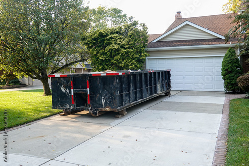 Long blue dumpster full of wood and other debris in the driveway in front of a house in the suburbs that is being renovated photo
