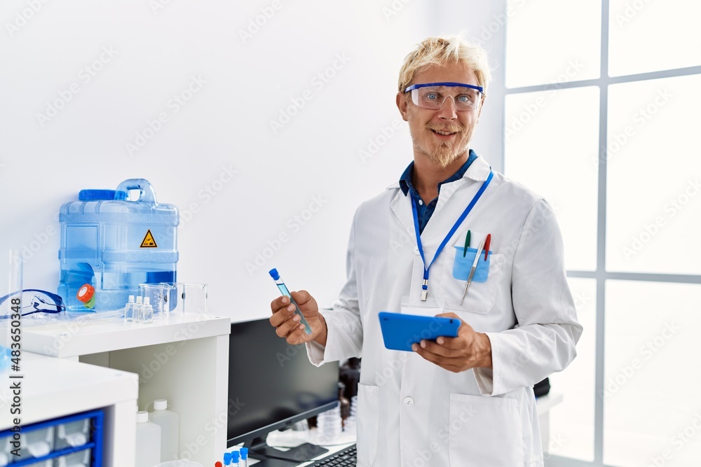 Young caucasian man wearing scientist uniform holding test tube and touchpad at laboratory Young caucasian man wearing scientist uniform holding test tube and touchpad at laboratory