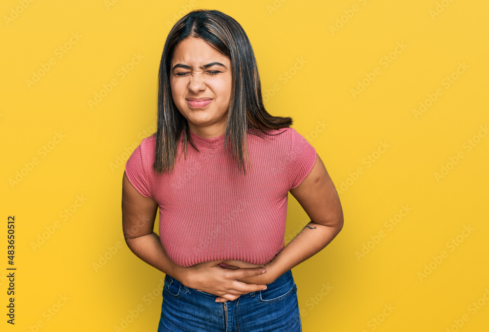 Young hispanic girl wearing casual t shirt with hand on stomach because nausea, painful disease feeling unwell. ache concept. Young hispanic girl wearing casual t shirt with hand on stomach because nausea, painful disease feeling unwell. ache concept.